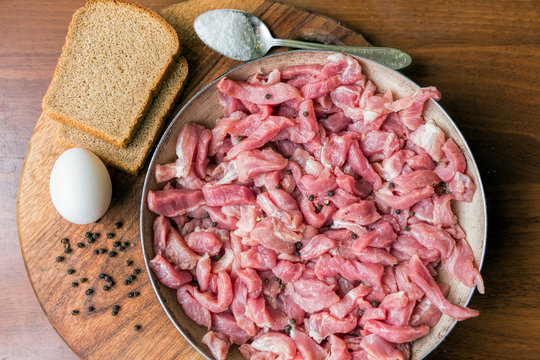 Raw sliced meat in a frying pan, bread, egg and spoon with salt
