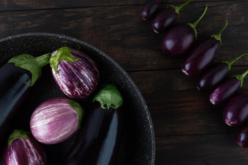 Eggplant varieties arranged creatively on frying pan and wooden table closeup. Top view.
