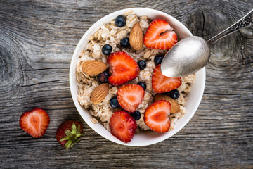 Oatmeal with almonds and berries in a  bowl on wooden background. Top view. Diet breakfast.