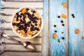 Top view of the oatmeal with almonds and berries in a  bowl on blue rustic  background. diet breakfast.
