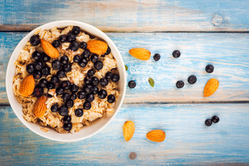Top view of the oatmeal with almonds and berries in a  bowl on blue rustic  background. diet breakfast.