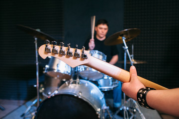 Fototapeta premium Guitar neck close-up on drum set background . Focus on guitar neck and guitar player hand, drummer playing on drums on background. Alive performance