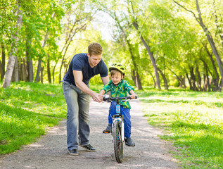 father teaches his son to ride a bike in park