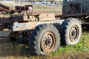 The old broken truck with two big lowered wheels against the village with agricultural machinery