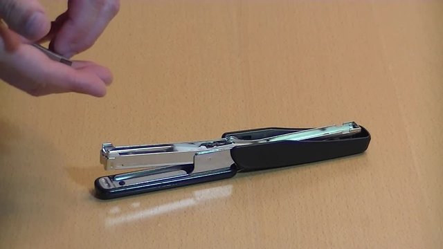 Hands add clips to an empty office black stapler