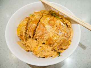 fried pork cutlet topped with egg on steamed rice in white bowl