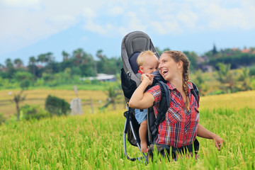 Nature walk in green rice terrace field. Happy mother hold little traveller in carrying backpack....