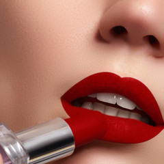 Extreme close up on model applying dark red lipstick. Make-up
