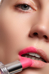 Close-up portrait of attractive lips of beautiful woman. Rouging her lips with pink mate lipstick. The lady is gently smiling. Close-up of woman applying pink lipstick on her lips

