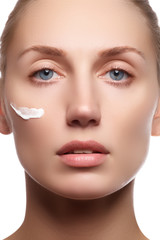 Beautiful face of young woman with cosmetic cream on a cheek. Skin care concept