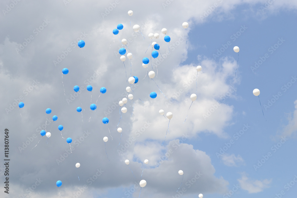 Wall mural balloons in the sky. flying white and blue balloons in a cloudy sky.