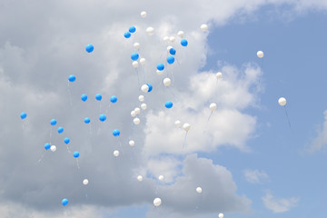 Balloons in the sky.
Flying white and blue balloons in a cloudy sky.