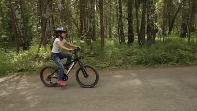 little girl rides her bike on a forest trail
