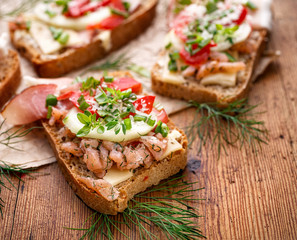 Sandwiches with homemade bread, containing fish, vegetables and fresh herbs on a wooden table