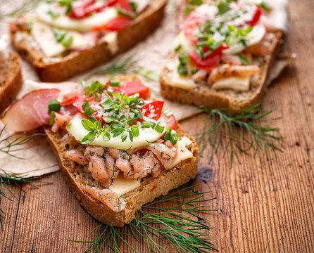 Sandwiches with homemade bread, containing fish, vegetables and fresh herbs on a wooden table