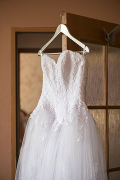 White wedding dress on a hanger in the room of the bride 
