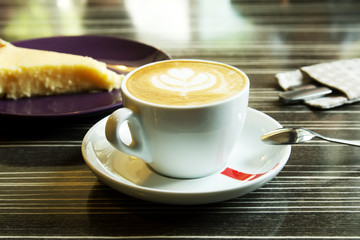 Morning cappuccino coffee and cheesecake. Cheesecake and kitchen appliances on the background. Coffee with art foam.