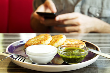 Homemade Salty Cheese Pancakes with sauce Pesto. Guy with the phone on the background. Pancakes photographed close.