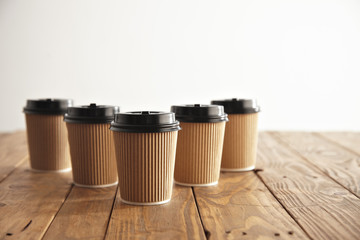 Five carton paper cups with black caps in row isolated on left side of rustic wooden table, top view