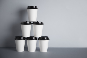 Pyramid made from six white take away paper cups with closed black caps, isolated on simple gray background on side
