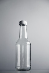 Empty unlabeled glass transparent bottle isolated on gray background in center