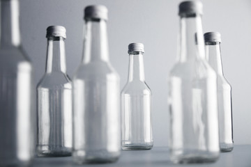 Set of empty cristal unlabeled bottles randomly presented on gray surface, isolated, close focus on backward bottles