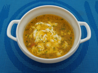 Delicious soup with homemade noodles and sour cream in a white bowl,which stands on a blue tablecloth