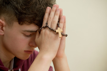 Teenage boy praying with a rosary - obrazy, fototapety, plakaty