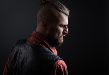 Side view of adult bearded man with hairstyle looking down against of black background
