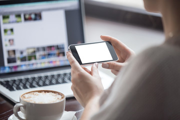 Female hands holding smartphone with empty blank screen for copyspace in coffee shop. Rear view. Woman sitting with cup of coffee and using electronic devices. Close-up