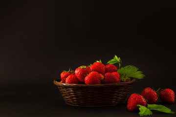 strawberries in a wicker basket on a black background. Toned dark photos.