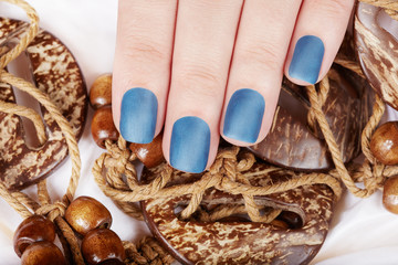 Hand with blue matte manicured nails and wooden necklace