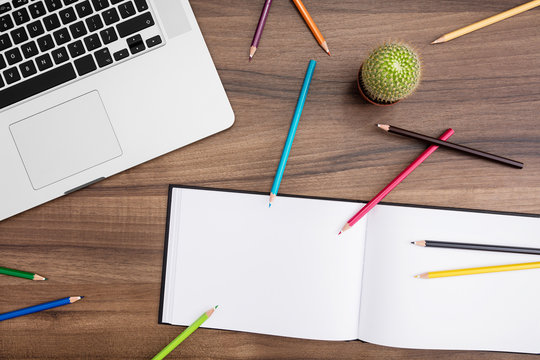 Desk with open laptop, cactus, notebook and pencils in many colors 