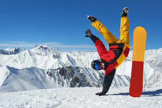Man standing on hand upside down near snowboard