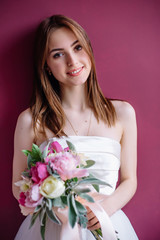 young beautiful bride with a bouquet of pink peony near the wall