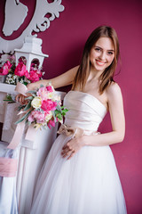 Fototapeta premium young beautiful bride with a bouquet of pink peony near the wall