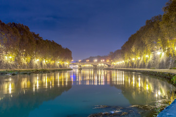 Fototapeta premium Old stone bridge on the river Tiber in Rome, lit at night