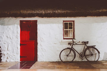 Traditional irish thatched cottage, with red wooden two parts door and an old bicycle © t0m15