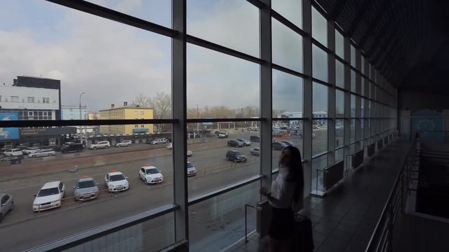 Business woman with luggage stands near windows in airport