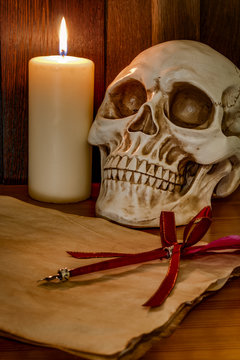 Candle lit scene of a skull, aged paper with a pentagram wax seal on it and a red feather fountain pen
