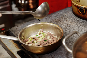 Chef is frying lamb slices with vegetables