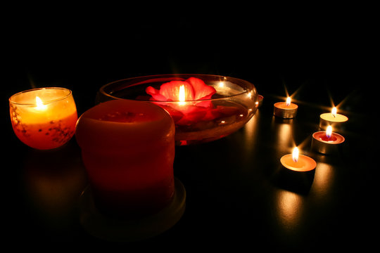 Teelichter und andere romantische Kerzen auf schwarzem Hintergrund verbreiten warmes Licht und angenehme Atmosphäre