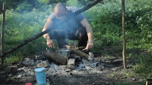 A man prepares tea on a campfire. Checks as a burning fire in early moning