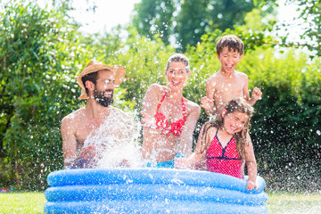 Familie spitzt mit Wasser im Garten Swimming Pool bei Abkühlung, Mutter, Vater und Kinder in einem...
