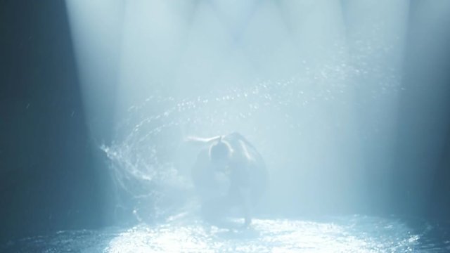 dancer does a break-dance in the water in a circle of light