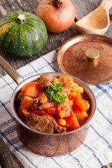 stew of beef with vegetables in a copper pot closeup