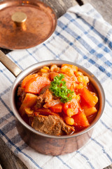 stew of beef with vegetables in a copper pot closeup