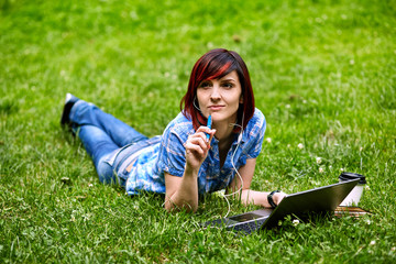 Naklejka na ściany i meble Beautiful young freelancer woman using laptop lying on the grass in the park.Happy smiling girl working online.Studying and learning using notebook computer.Freelance work,business people concept.