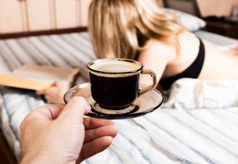 beautiful woman reading a thick book lying on the bed, close-up coffee cup