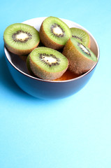 Slices of kiwi fruit on bowl on blue background viewed from abov